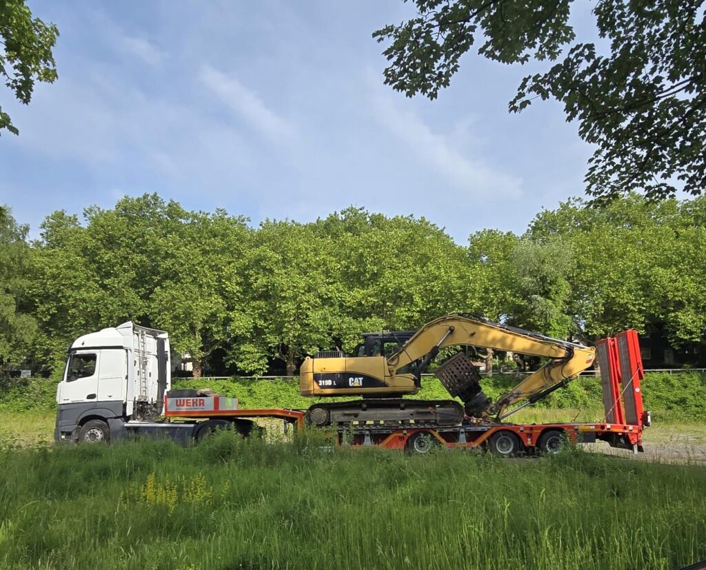 Ein weisser Sattelzug transportiert einen gelben CAT Bagger auf einem Tieflader